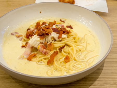 Close up the spaghetti with garlic bacon on a white plate on a wooden table.の写真素材