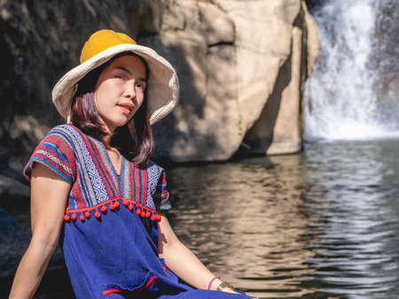Women wear traditional Thai costumes and yellow hats. Sitting by the waterfallの写真素材