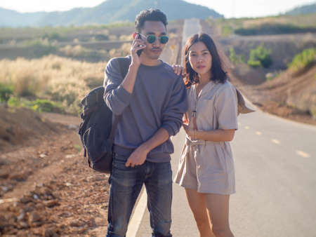 A man carrying a bag and talking on the phone and standing on the roadside with a womanの写真素材
