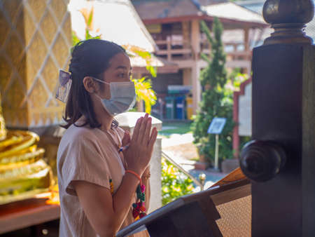 A woman wearing a mask is writing on an orange cloth as part of Buddhism.の写真素材