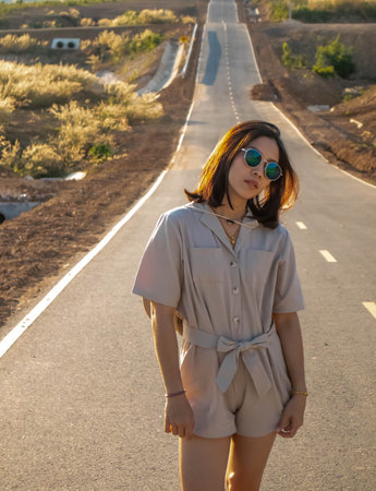 A woman wearing a hat and glasses is standing in the middle of the road.の写真素材
