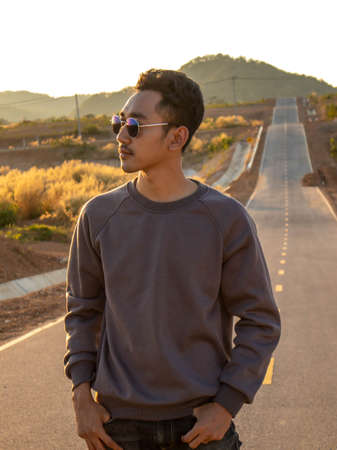 A man wearing a glasses is standing in the middle of the road.