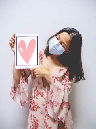 A woman wearing a mask and holding a heart shaped tablet.