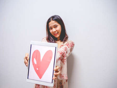 A woman wearing a pink dress and holding a tablet with a heart