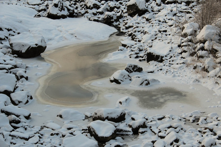 Frozen riverbed with snowy rocks in winterの写真素材