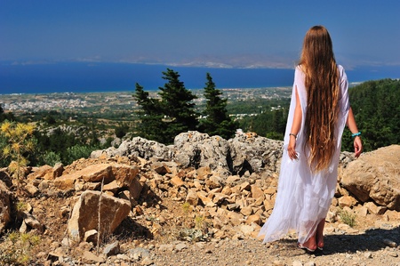 Beautiful long-haired girl looking afar from the mountainの写真素材