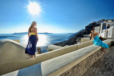 Two young women take a photo of each other in the town of Fira, Santorini island, Greeceの写真素材