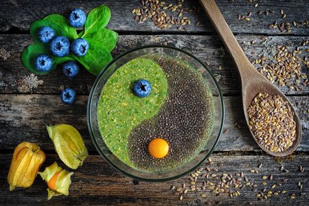 Healthy breakfast. Raw flaxseed porridge with chia seeds, spinach, physalis and fresh blueberries on wooden table, top view. Clean eating, dieting, vegetarian food conceptの写真素材