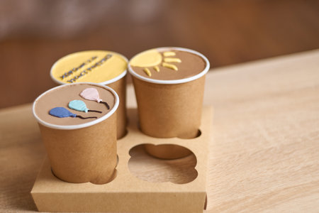 three homemade mini chocolate cake to go in coffee cup with cream drawing on a table, new confectionery trend concept. Paper cups with cakey are in a box. fashionable dessert. Horizontal, copy spaceの写真素材