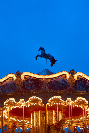 horse on the top of roundabout, galloper. Childrens Carousel close up in the night illumination. Outdoor vintage colorful luminous. Retro Shiny Carousel details, horses. vertical photo, bottom viewの写真素材