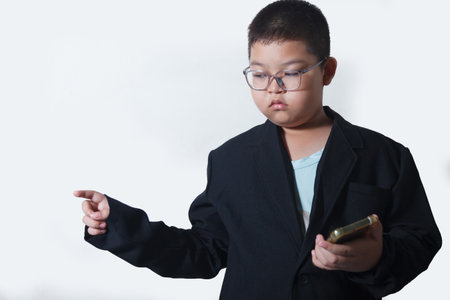 A young Asian boy in a suit and glasses is using a mobile phone, pointing his finger to the right against a white background.の写真素材