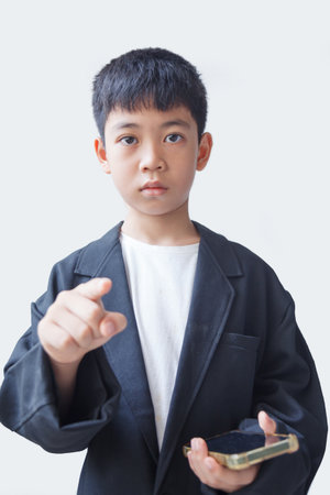Little asian boy holding mobile phone and pointing at camera isolated on white backgroundの写真素材