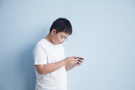 A young Asian boy has a serious expression and is oblivious to his surroundings while playing on his smartphone.の写真素材