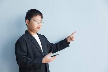 A young businessman in a suit holds a smartphone in his right hand and points to an empty space with...