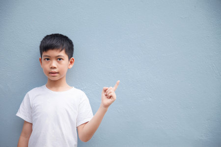 An Asian boy wearing a white shirt is pointing to the side in the blank space for text.