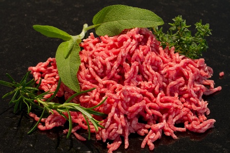 raw minced meat on black background with salvia, rosmary and thyme