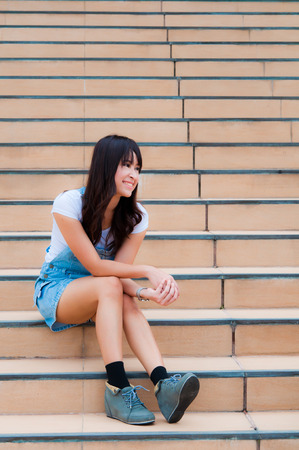 An asian woman in short jean smile and sit on the staircaseの写真素材