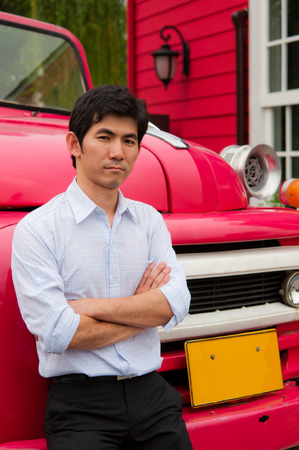 An asian man cross his arm and lean against pink truckの写真素材