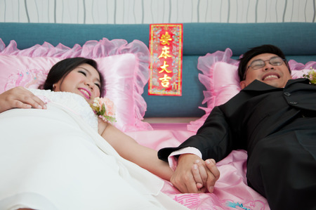Bride and groom hold their hand and lay on the bed which beleive that they will live together till they die as Chinese Traditionalの写真素材