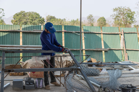 Petchaburi, Thailand - February 20, 2016: One man worker cut iron frame for making fence at prepared...