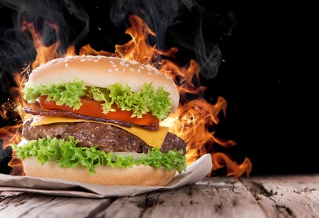 Delicious hamburger with fire flames on wooden background