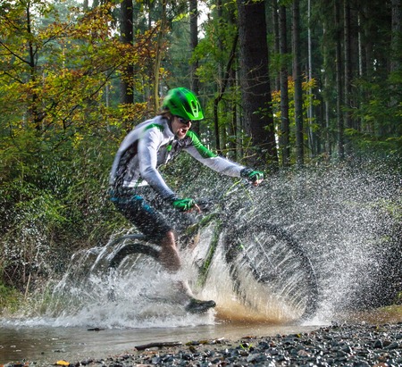 Mountain biker speeding through forest stream. Water splash in freeze motion.の写真素材