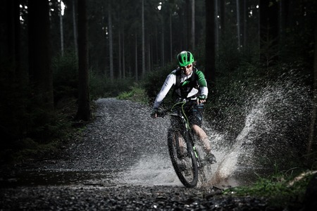 Mountain biker speeding through forest stream. Water splash in freeze motion.