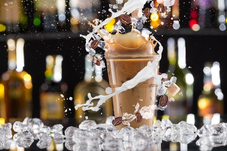 Cold coffee drink with ice, beans and splash, close-up.