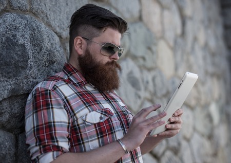Handsome big moustache hipster man in the city with tablet.の写真素材