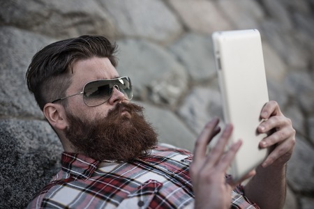 Handsome big moustache hipster man in the city with tablet.