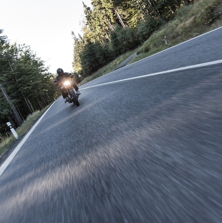 Man seat on the motorcycle on the forest road during sunrise.の写真素材