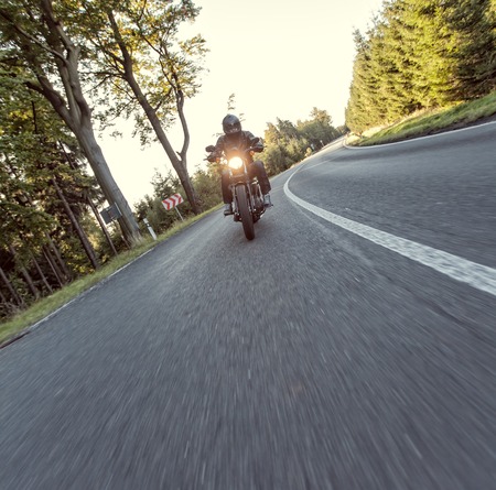 Man seat on the motorcycle on the forest road during sunrise.の写真素材