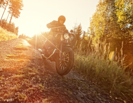 Man seat on the motorcycle on the forest road during sunrise.の写真素材