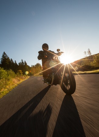 Man seat on the motorcycle on the forest road during sunrise.の写真素材