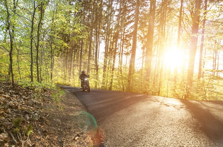Man seat on the motorcycle on the forest road during sunrise.