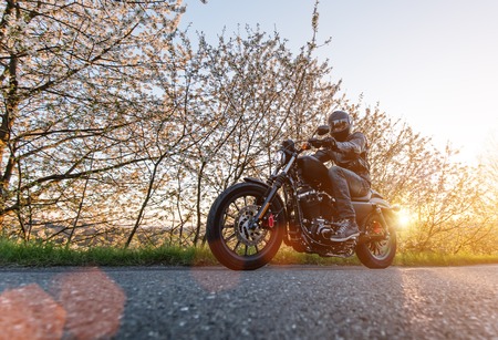 Man seat on the motorcycle on the forest road during sunrise.の写真素材