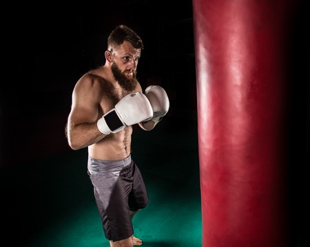 Muscular hipster fighter giving a forceful kick during a practise with a boxing bag. Kickboxing.の写真素材