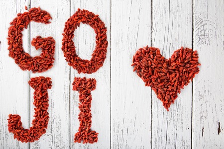Goji berries as a heart and letters on old white wooden table, top view.の写真素材