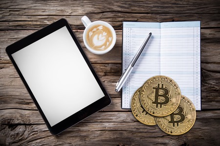 Bitcoin gold coins with empty paper, coffee cup and tablet. Virtual cryptocurrency concept.の写真素材