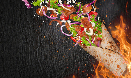 Close-up of kebab sandwich with flying ingredients with fire flames background.の写真素材