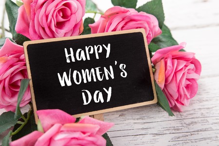 Small chalkboard for Women's day. Background with pink roses on old wooden table.の写真素材