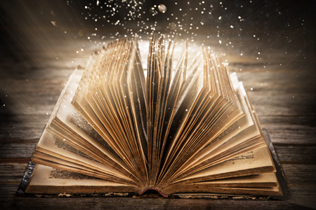 Old open book on wooden table with mystic magic bright light.の写真素材