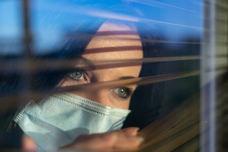 Woman with veil looking out of home window, concept of quarantine during viral pandemic.の写真素材