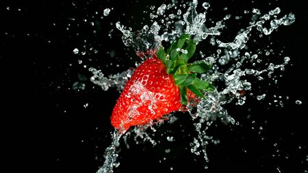 Freeze motion of fresh strawberry with splashing juice isolated on black backgroundの写真素材