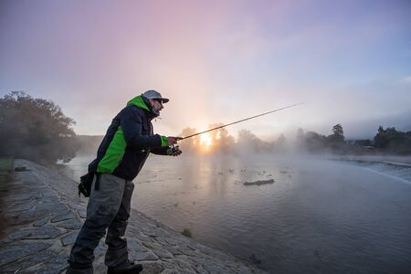 Men fishing in river with fly rod during summer morning.の写真素材