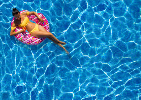 beautiful woman sitting in inflatable donut at swimming pool