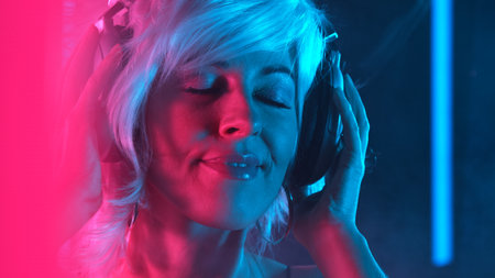 Happy young woman with silver headphones dance in neon lights.の写真素材