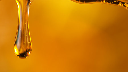 Pouring oil or honey drop on golden background.の写真素材