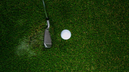 Golf club hitting golf ball on green grass.