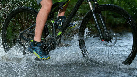 Sportsman riding bicycle in the shallow stream and splashing water.の写真素材